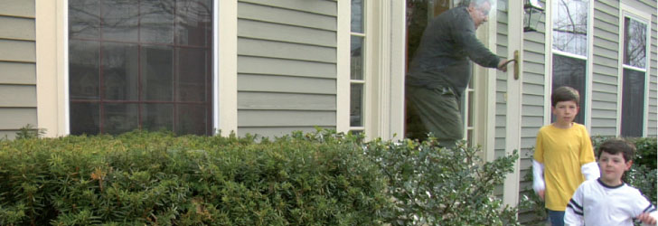 Two small children exiting a house through the front door with grandparent close behind
