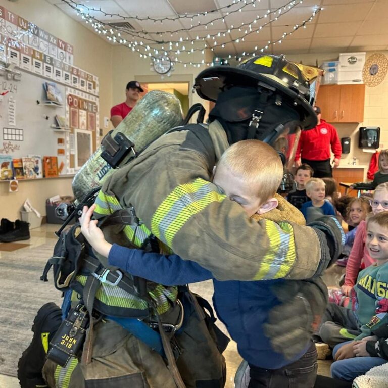 firefighter in protective work gear receiving a hug from an elementary school aged child